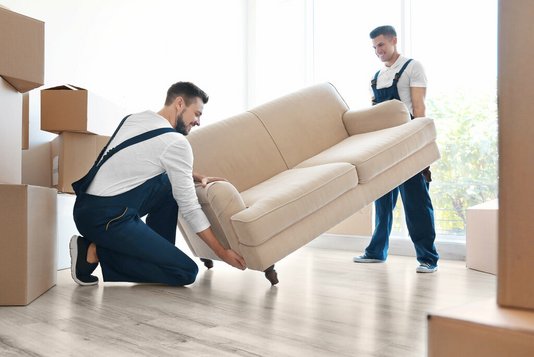 umzug-auszug-einziehen-karton-haus-07 Zwei Umzugshelfer tragen eine Couch